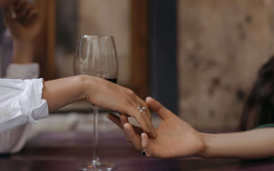 A couple holding hands with a clear wine glass at the back.
